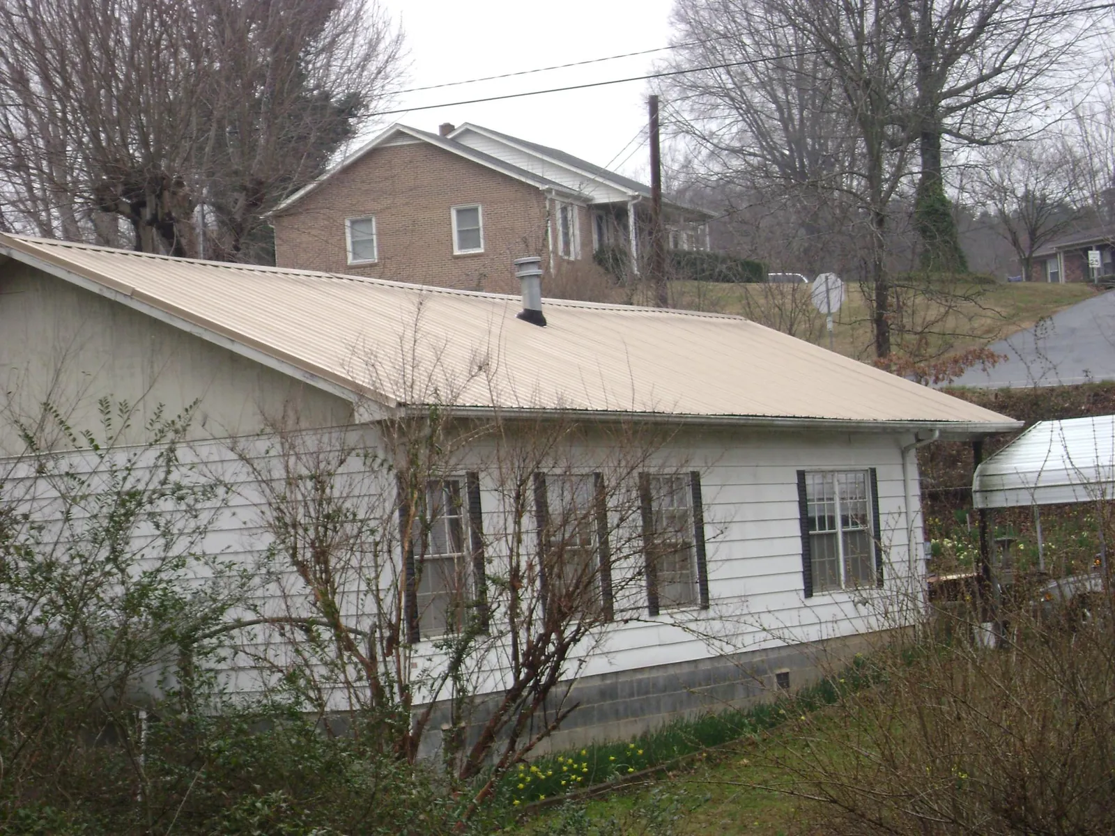 Tan metal roof on a white sided house set into a hillside — Commercial Roofing by Roofing Brothers in New Washington